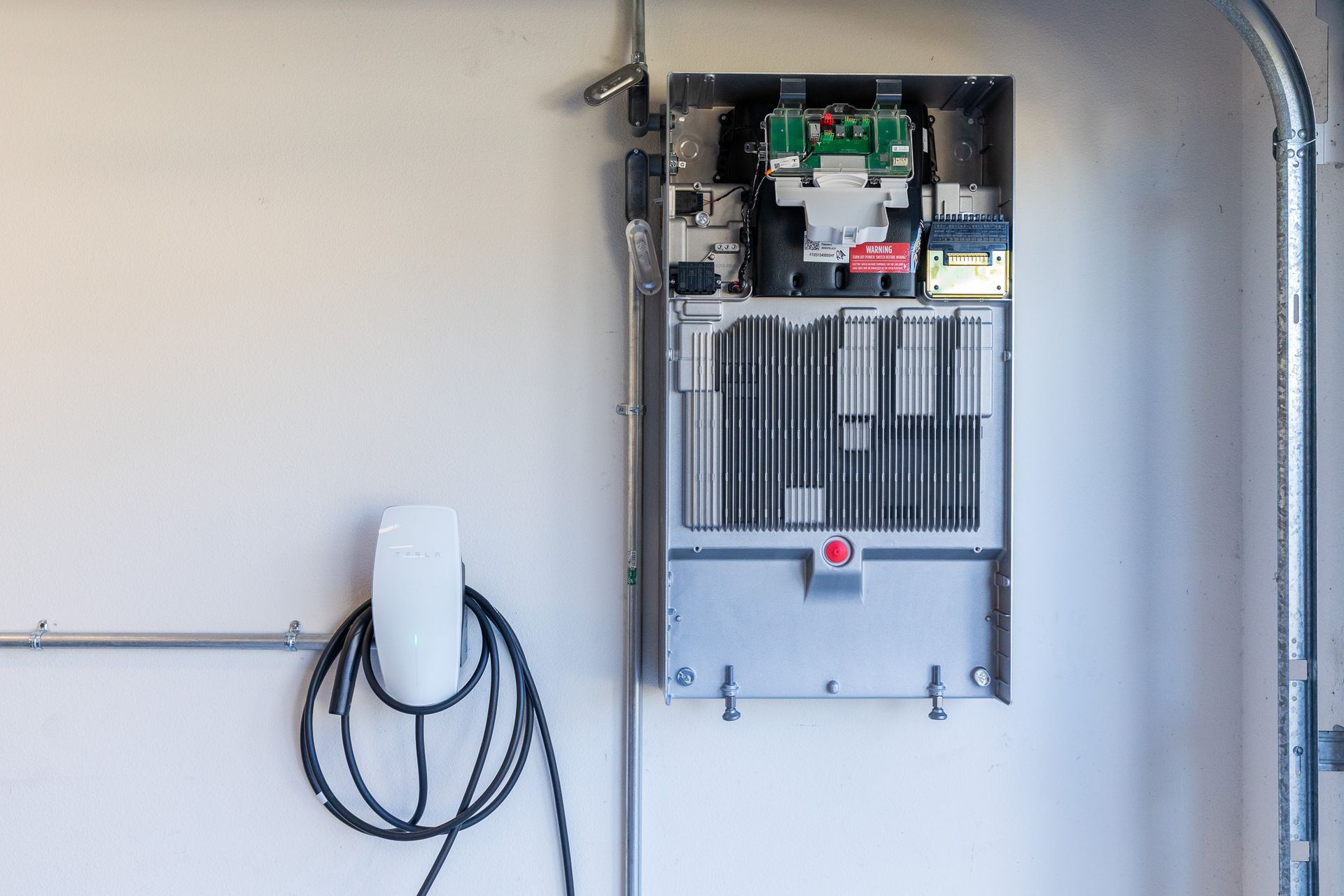 Wall-mounted electrical control panel in a garage with a coiled cable and conduit pipes