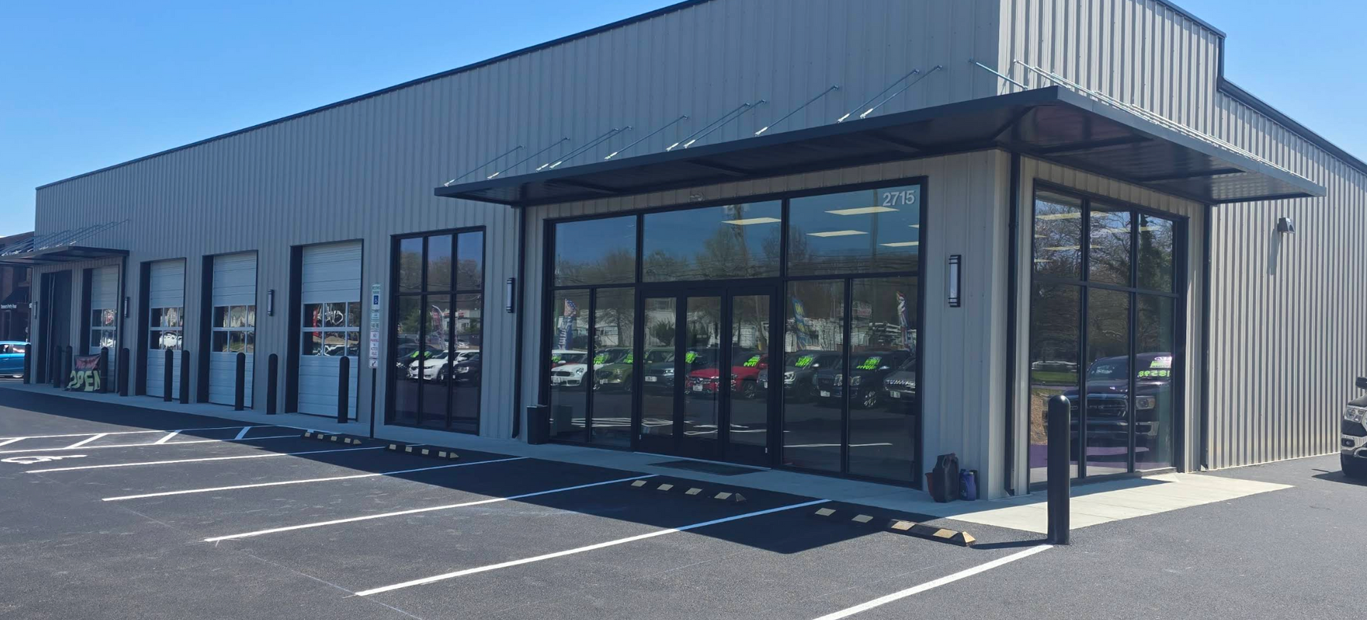 Modern gray commercial building with large windows and a covered entrance in a parking lot | Harford Auto Gallery