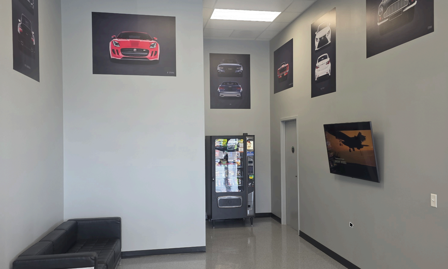 Modern showroom hallway with wall-mounted car art, a black bench, and a vending machine at the end. | Harford Auto Gallery
