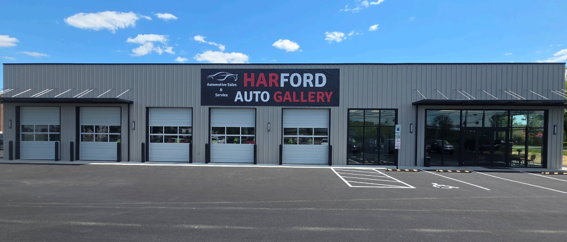 Harford Auto Gallery storefront with gray facade, red and black sign, and garage doors under a blue sky | Harford Auto Gallery