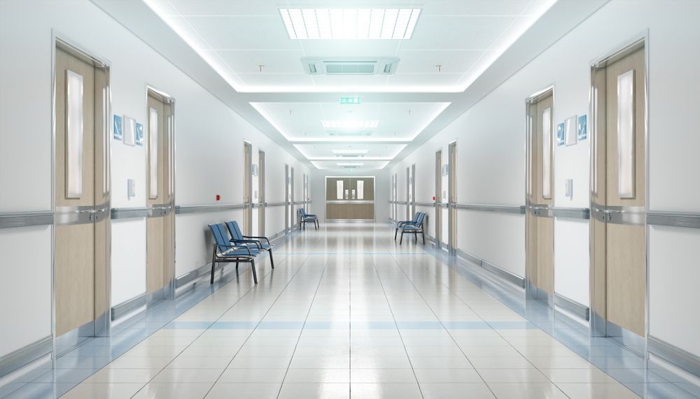Bright empty hospital corridor with white walls, blue trim, and chairs along the sides