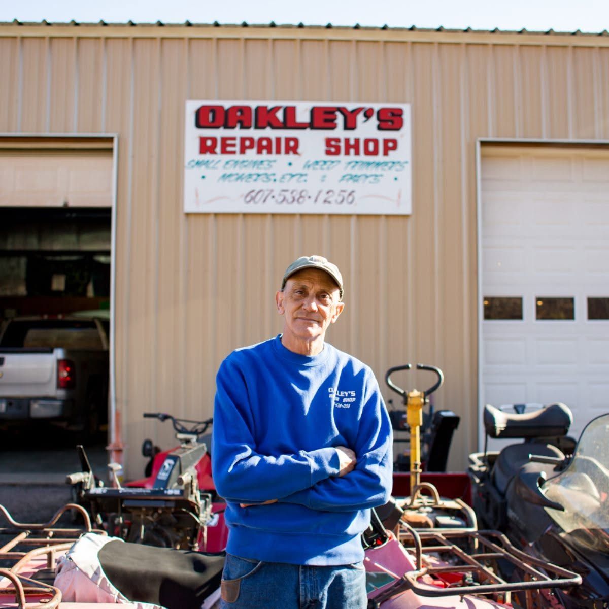 Man standing in front of Oakley’s Repair Shop with bicycles and tools outside.