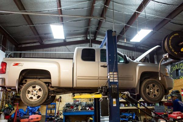 White pickup truck lifted on a hydraulic garage hoist inside an auto repair shop