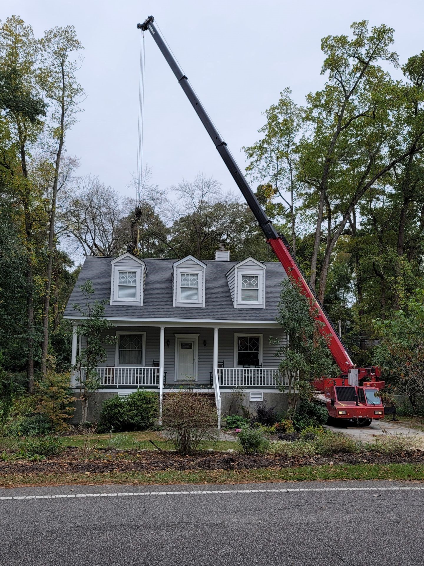 Crane lifting a red boom over a gray house with a front porch and dormer windows