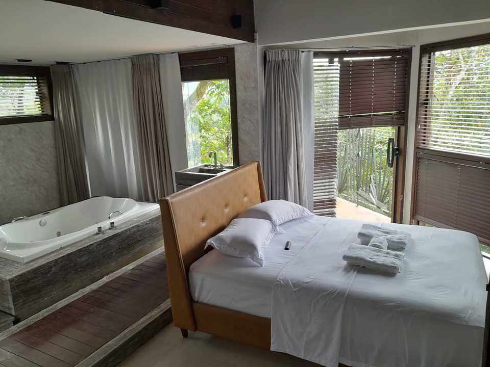 Um quarto de hotel de luxo com uma cama branca com cabeceira bege e uma banheira de hidromassagem embutida em uma plataforma de madeira.