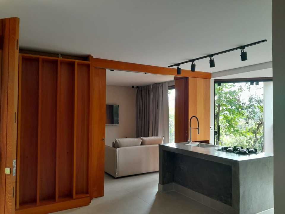 Uma sala de estar e cozinha modernas com painéis de madeira, uma ilha de concreto com fogão e um sofá bege.