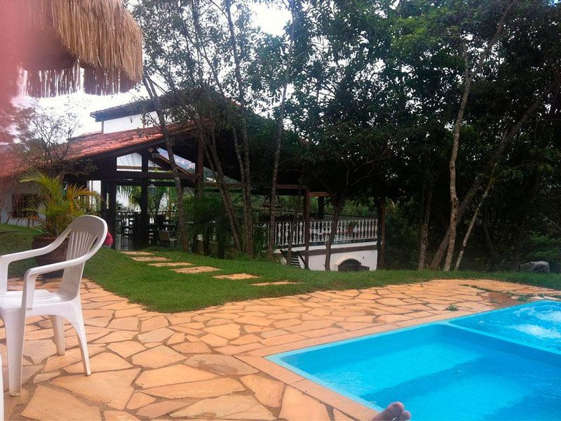 Uma piscina em um gramado, com uma cadeira branca em um pátio de pedra e uma estrutura coberta atrás dela.