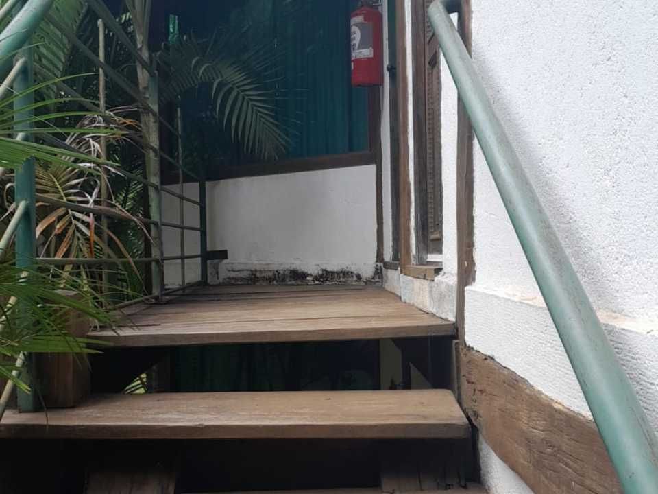 Escada externa de madeira com corrimão de metal verde, que leva a um pequeno patamar com um extintor de incêndio vermelho.