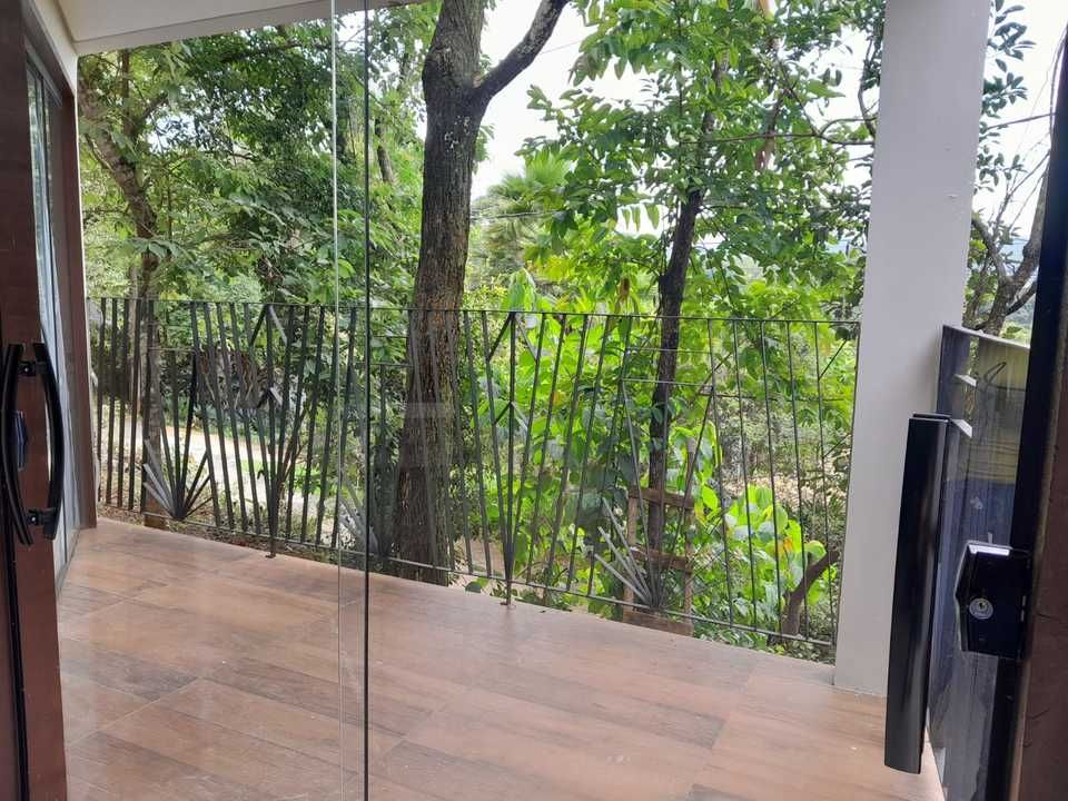 Um piso de madeira na varanda que dá para uma cerca de metal com vista para árvores verdejantes, visível através de uma porta de vidro aberta.