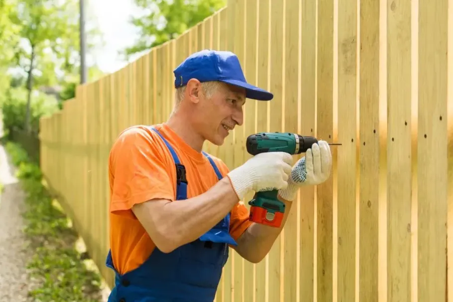 Worker using drill on wood fence.