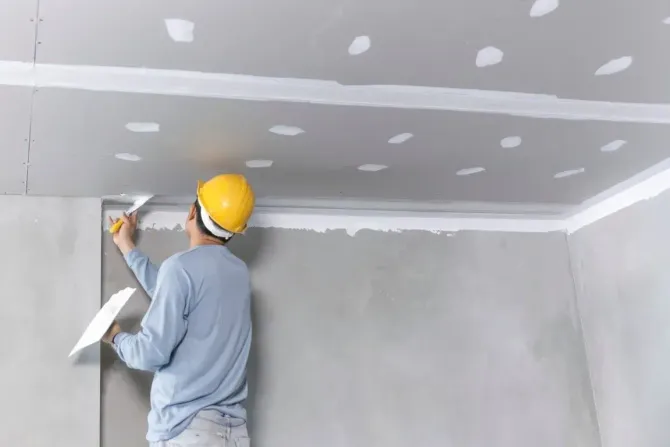 Construction worker applying joint compound to drywall ceiling.