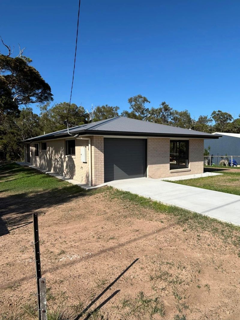 A Beige Brick House with A Gray Garage Door and Driveway — Country to Coast Homes In Gregory River, QLD