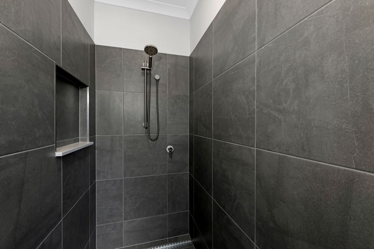 Dark Gray Tiled Shower with A Built-In Shelf and A Showerhead — Country to Coast Homes In Bundaberg, QLD