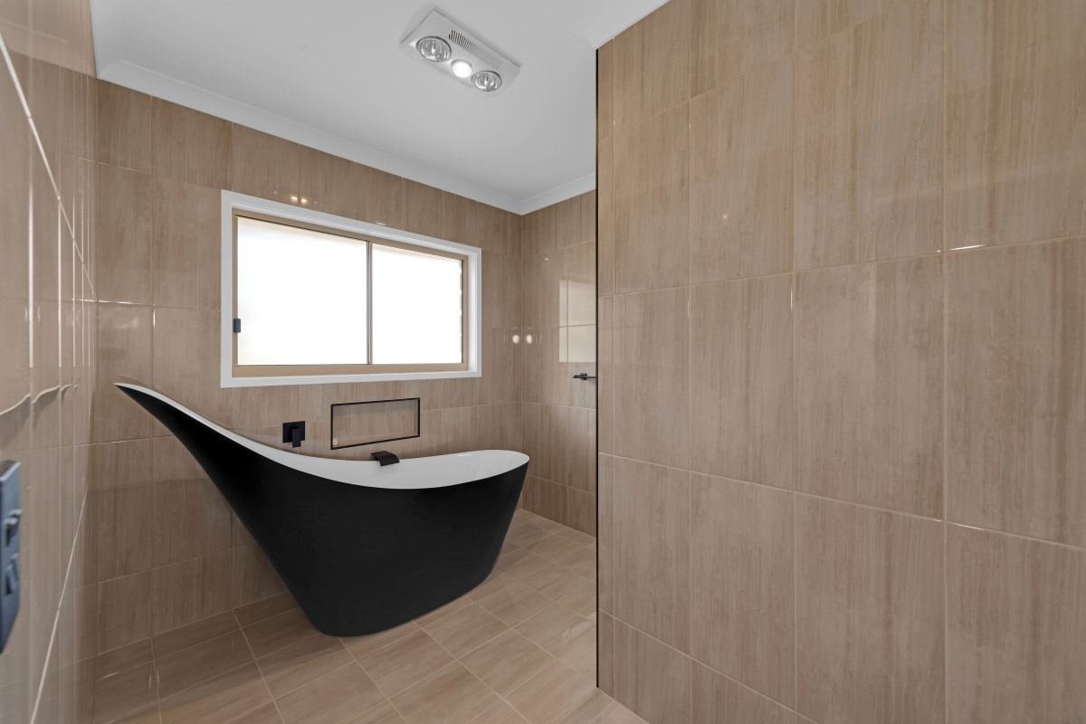A Bathroom with A Black, Curved Bathtub, Beige Tiled Walls — Country to Coast Homes In Gregory River, QLD