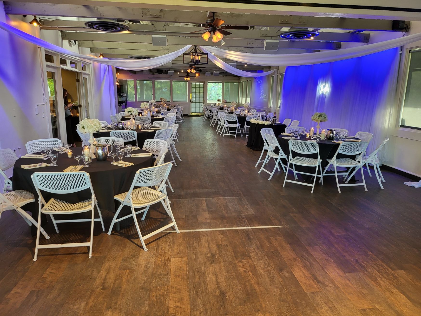 Empty banquet hall with round tables, white chairs, and blue-purple uplighting on the walls.