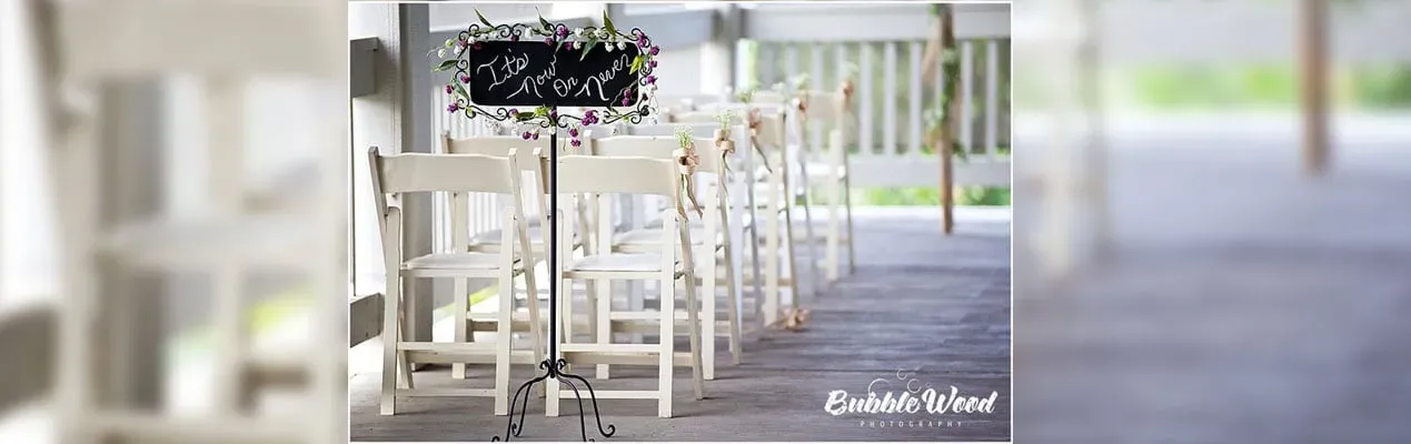 White chairs and tables lined along a bright covered walkway with a floral centerpiece.