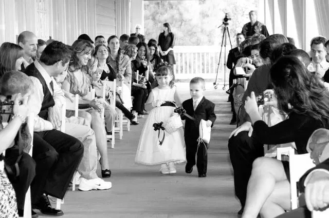 Flower girl walking down aisle at a wedding ceremony, guests seated on both sides and watching