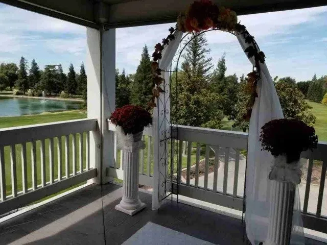 Decorated white gazebo overlooking a lake, with floral arch and draped fabric for an outdoor wedding ceremony