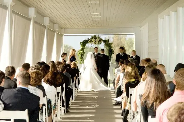 Wedding ceremony in a white chapel, bride and groom at the altar with guests seated on both sides