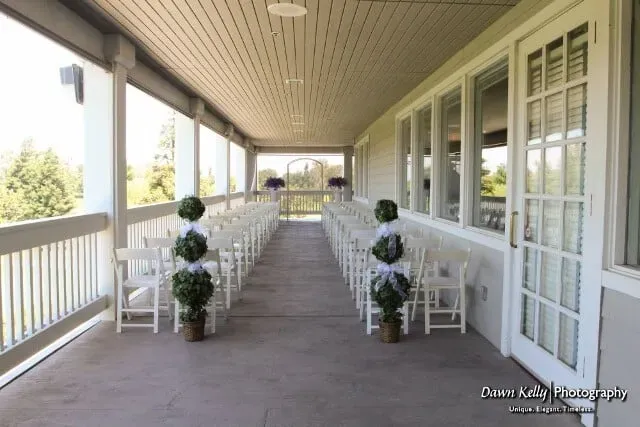 White porch walkway with white railings, potted topiary plants, and benches on both sides