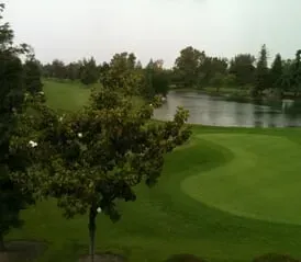 Golf course with green fairways, trees, and a pond under an overcast sky