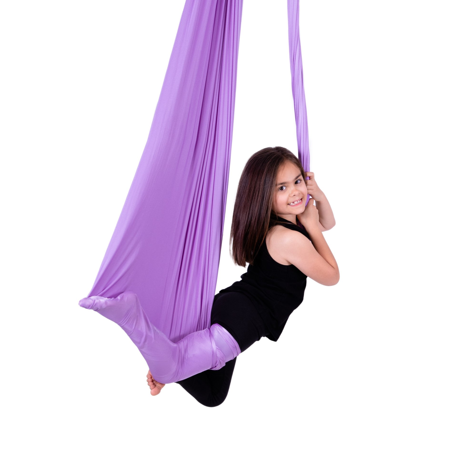 A young girl hanging from a purple aerial silk, smiling and enjoying the activity in a bright studio filled with wooden flooring.