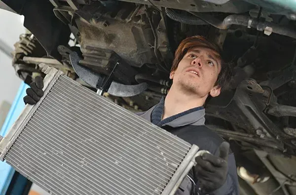 A Man Is Holding a Radiator Under a Car — Wyong Radiator Repairs in Tuggerah, NSW