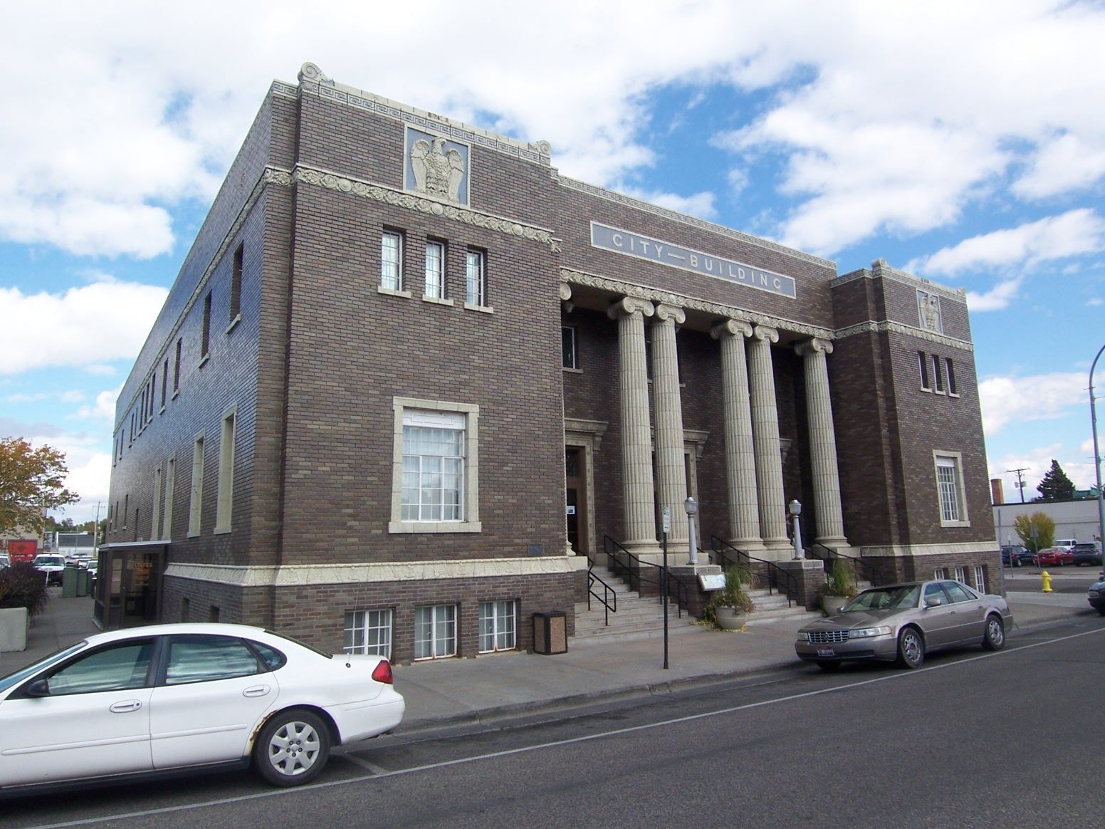 Brick building with white columns and parked cars. Blue sky background.