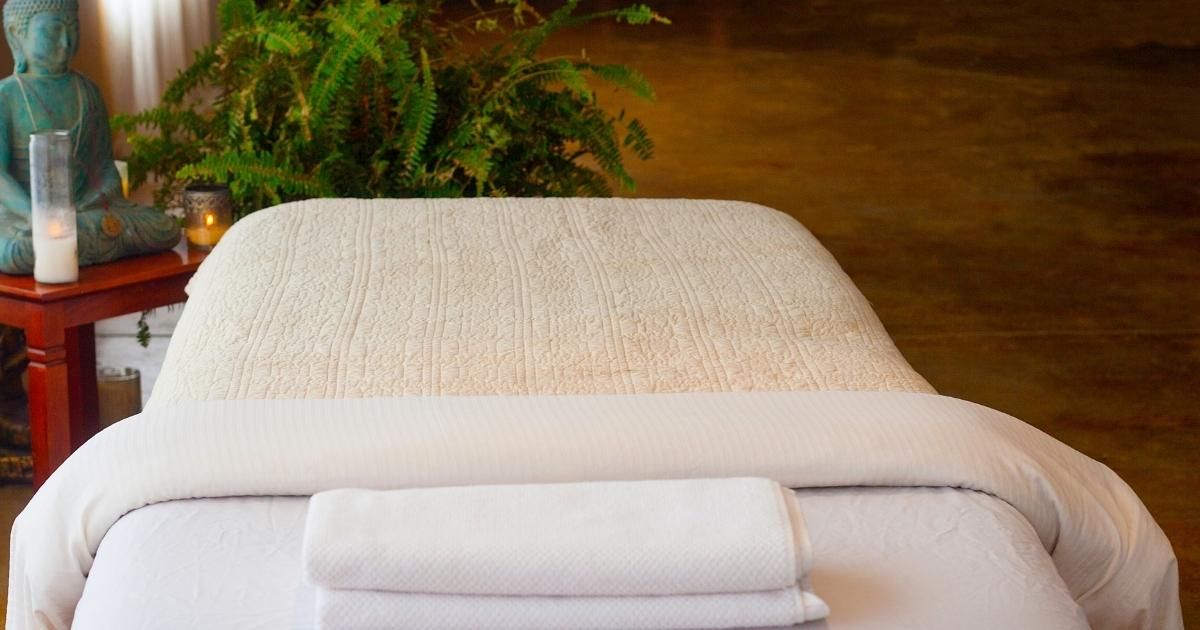 Massage table with white linens, a Buddha statue, and greenery.
