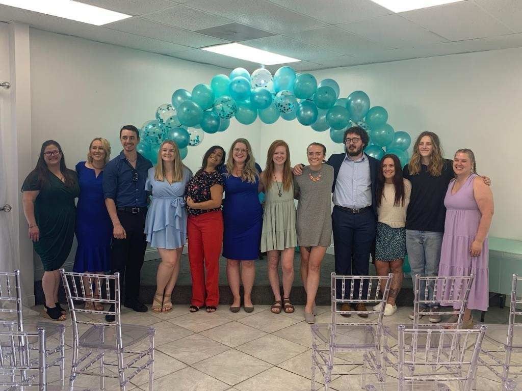 A group of people are posing for a picture in a room at Kansas City Massage Institue with balloons.