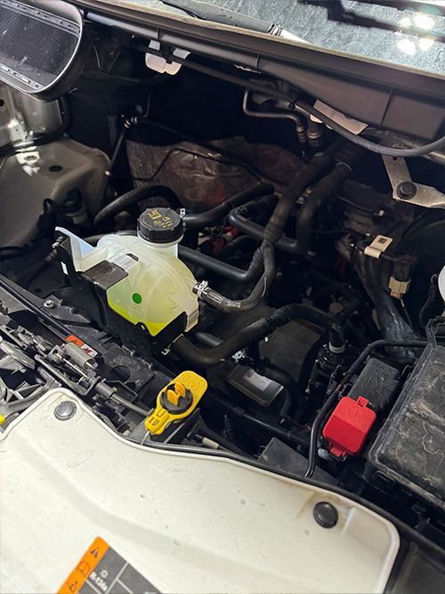 Engine compartment of a vehicle, showing coolant reservoir, hoses, and engine components  | S&C Automotive Inc