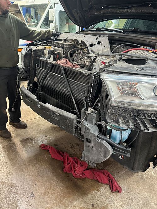 Man working on a car with the hood open. The car's front bumper is removed. Tools and a red cloth are visible  | S&C Automotive Inc