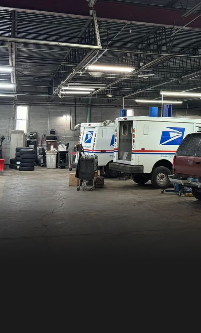 Inside a vehicle repair shop, postal service trucks are parked, worker | S&C Automotive Inc