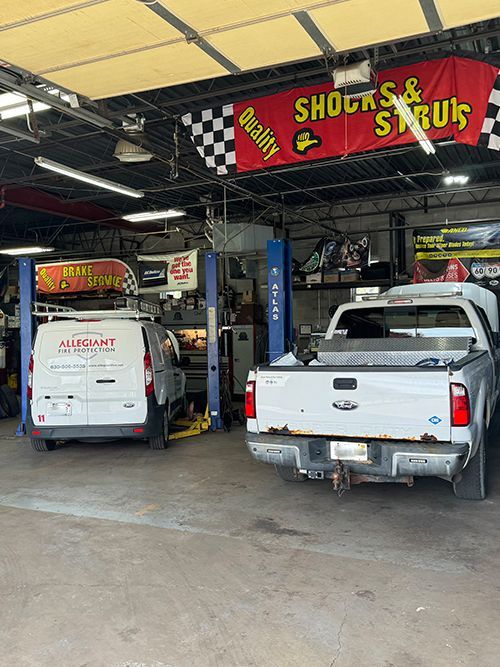 A repair shop interior with a white van and pickup truck on lifts. 