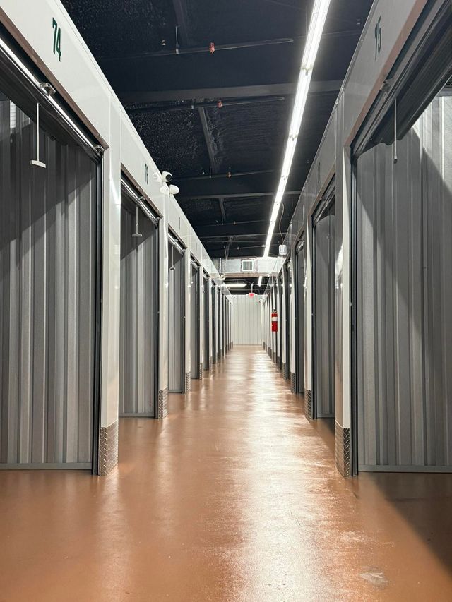 Interior of storage units; metal doors line a corridor with brown floor.