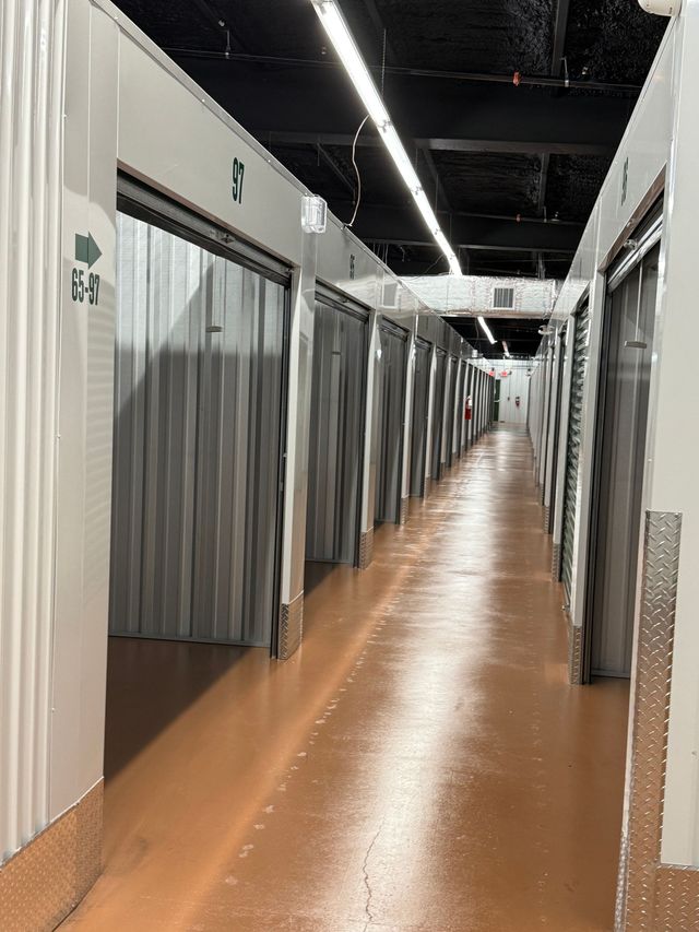 Interior view of a storage facility hallway with many metal unit doors and orange flooring.