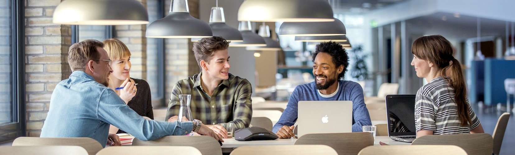 Coworkers discussing around a laptop at a conference table in a modern office