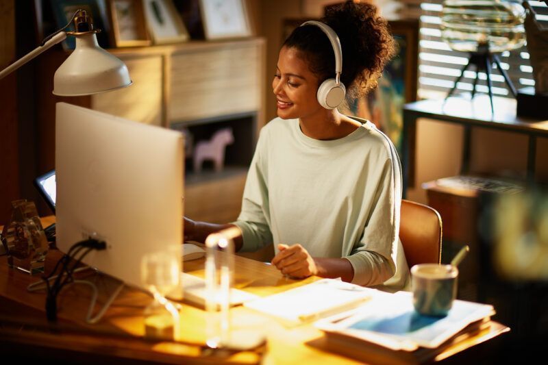 Person working at a desk with a desktop computer, wearing headphones in a warm home office
