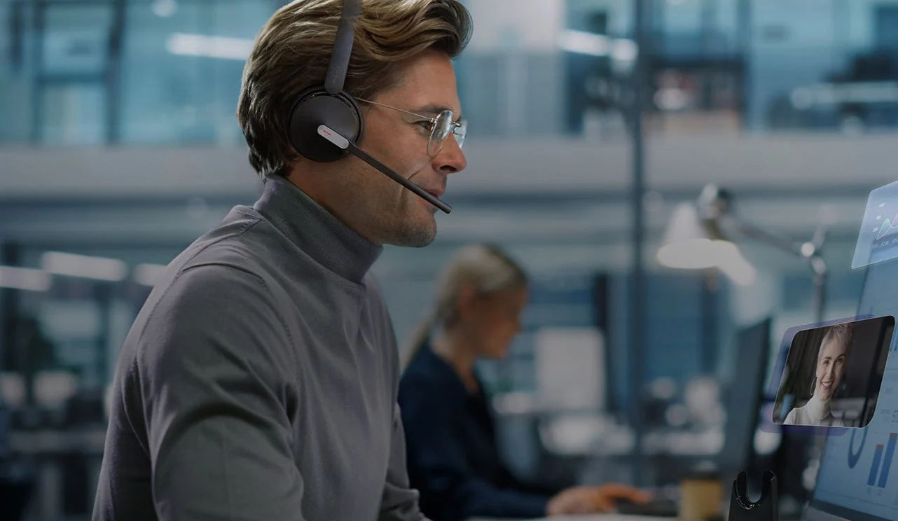 Man wearing a headset working at a computer in a busy office setting