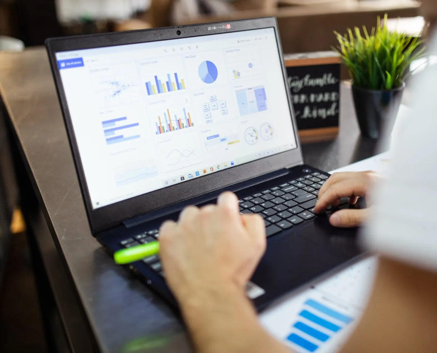Hands typing on a laptop showing analytics dashboards in a bright office