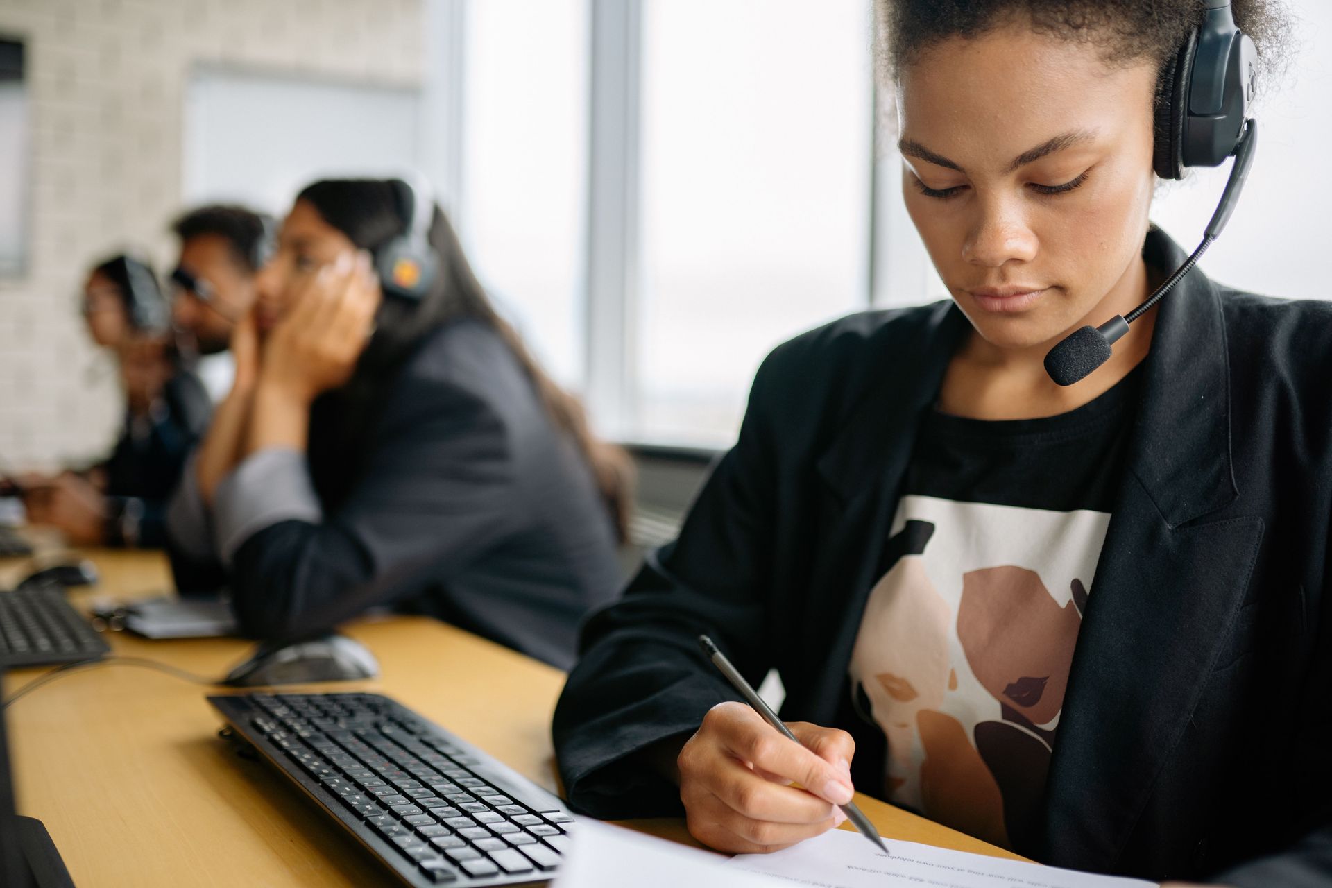 Person wearing a headset works on a laptop at a desk near a window.
