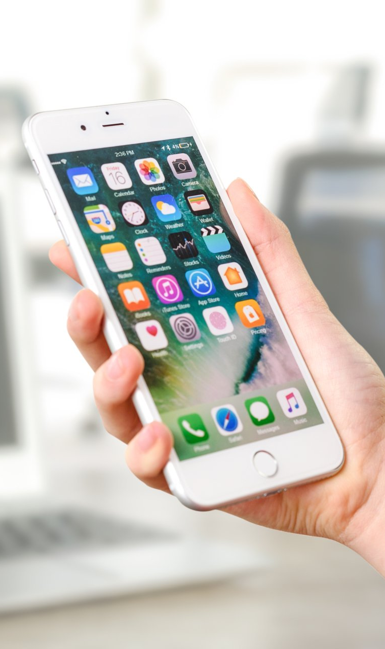 A hand holding a white smartphone with a colorful app screen, indoors.