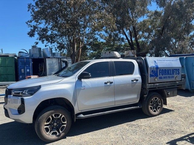 Silver Toyota Hilux truck with a utility body, parked outdoors. 