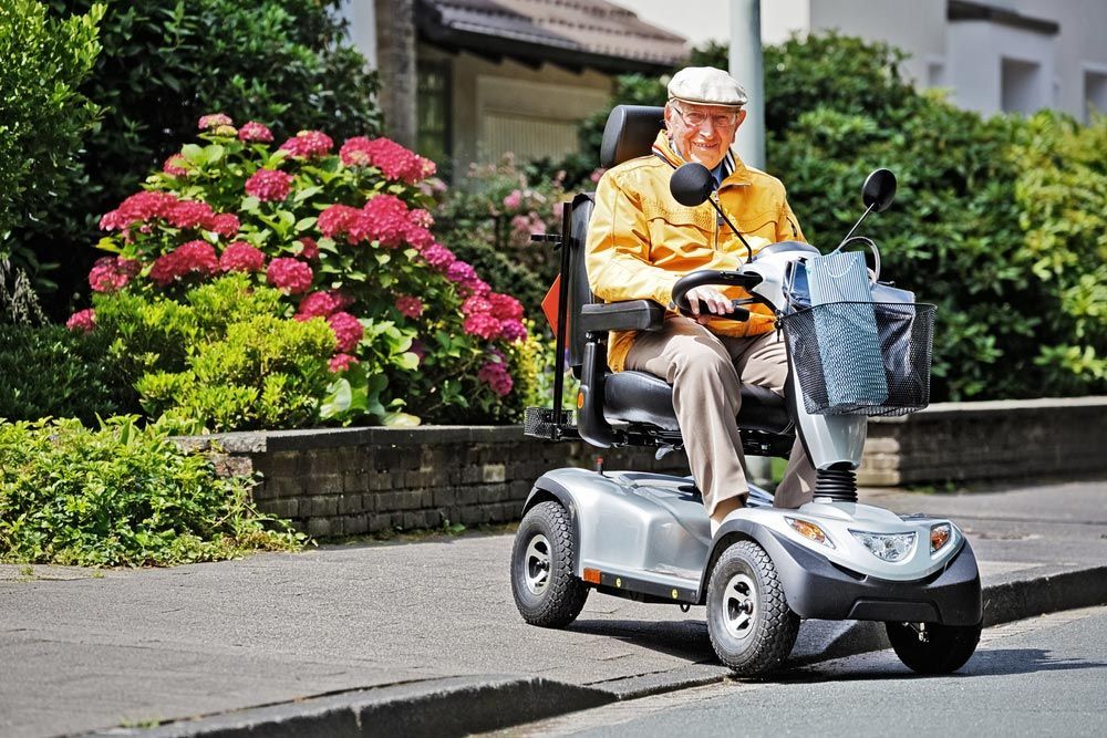 An Elderly Man Is Riding a Mobility Scooter Down a Street — Mobility Modification Services In Garbutt, QLD
