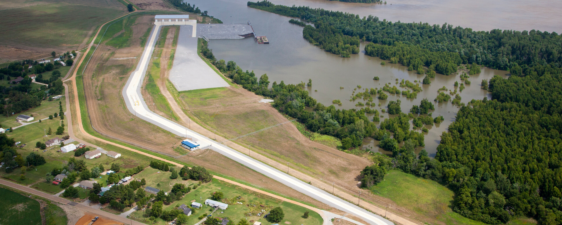 Aerial view of a riverfront embankment road beside a wooded river and homes