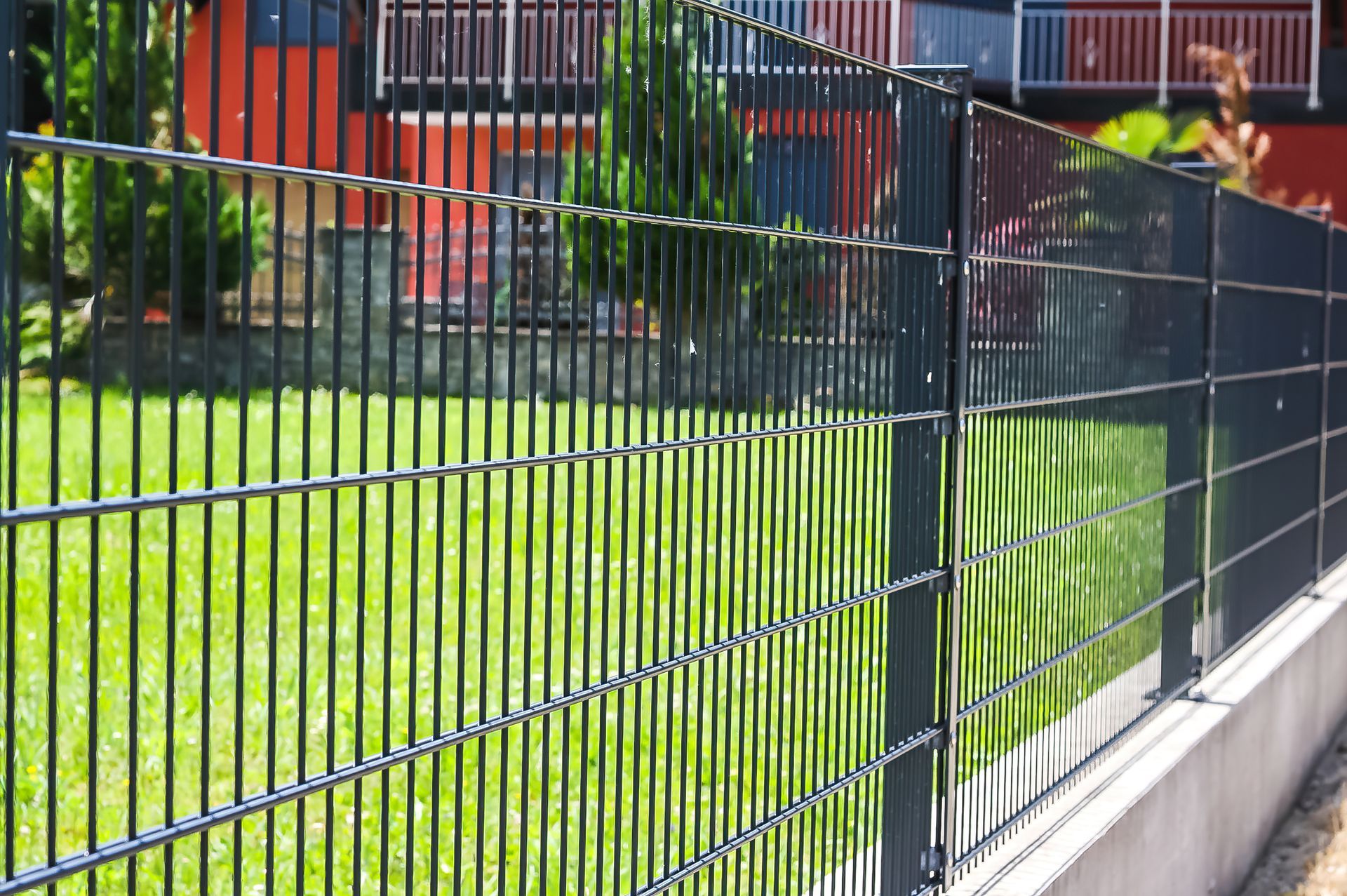 Black double-wire mesh security fence panel along a green lawn.