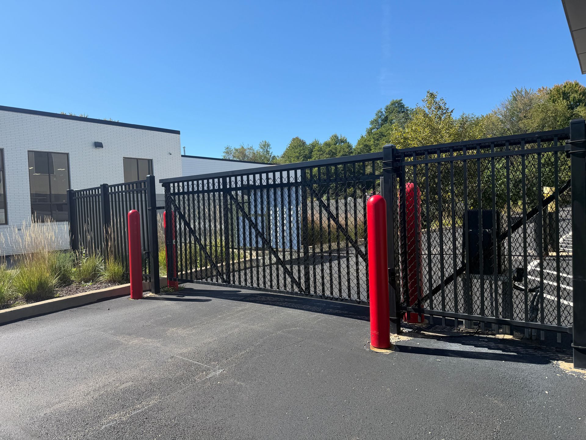 Black metal gate with red bollards at a paved industrial entrance under a clear blue sky
