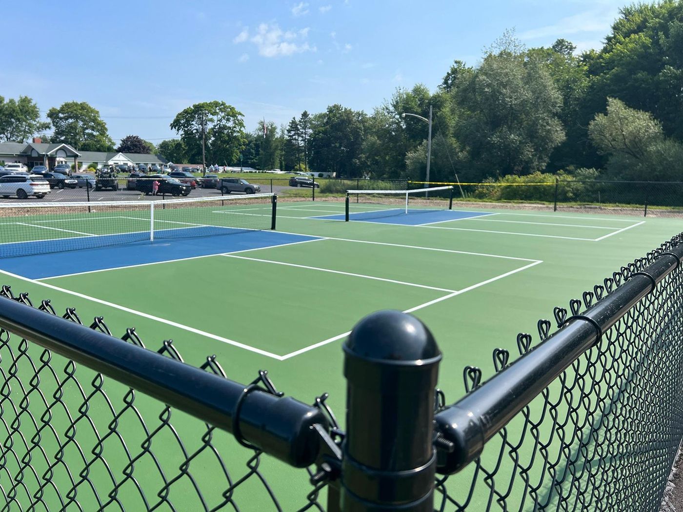 Empty green tennis court behind a chain-link fence under a clear blue sky