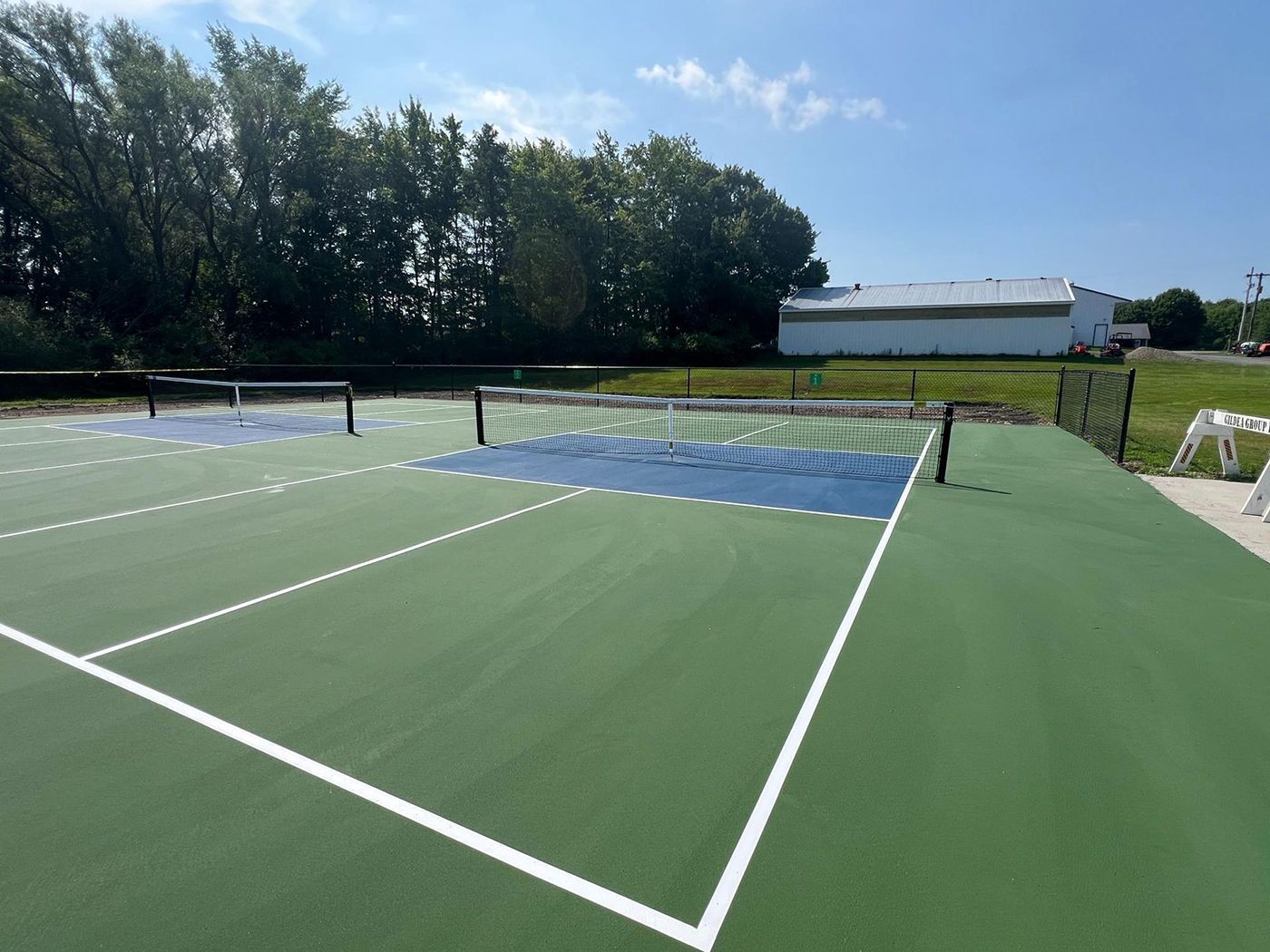 Empty green tennis court with white lines, net, and trees under a sunny sky
