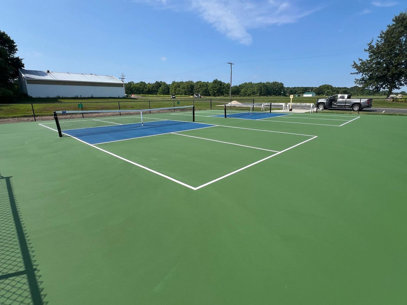 Outdoor pickleball court with green surface, white lines, and blue netted playing area under a clear sky
